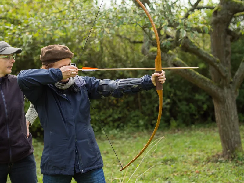 Frau beim Zielen auf eine Zielscheibe, im Hintegrund die Trainerin